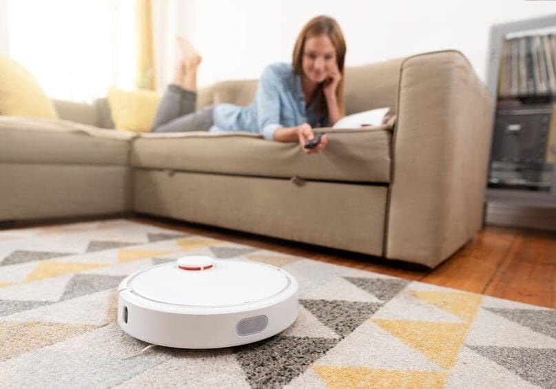 110195522_s-1 Woman relaxing while robot vacuum cleans floor.
